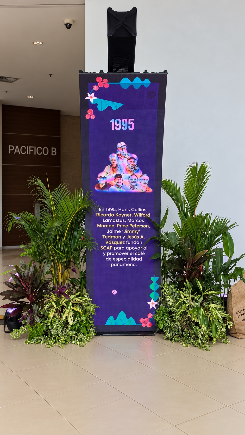 Detalle del montaje de plantas tropicales junto a una pantalla de World of Coffee